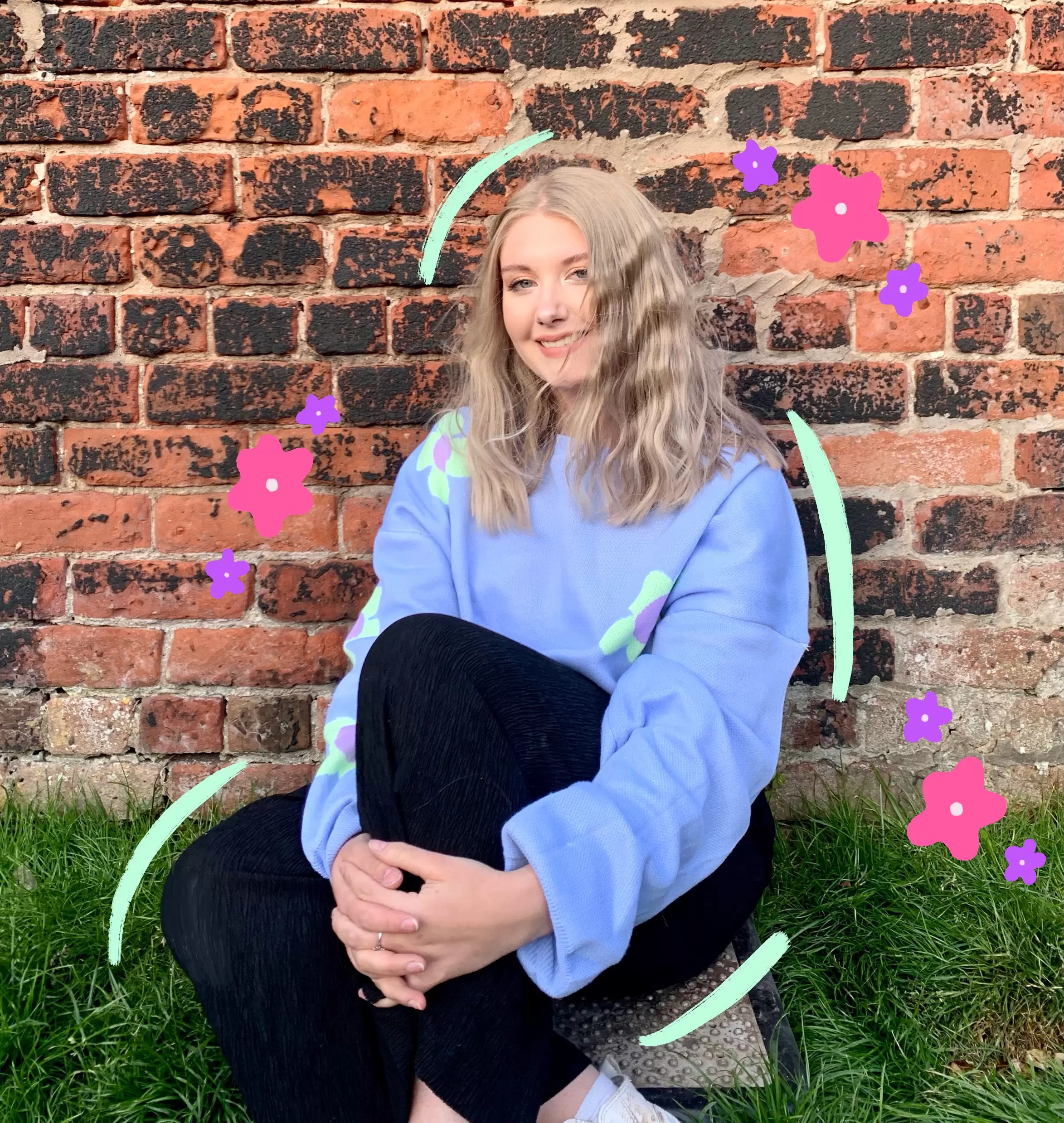 Chelsea, the founder of Purcell Green Studios. Sat on grass in front of a brick wall with flower doodles around the image.