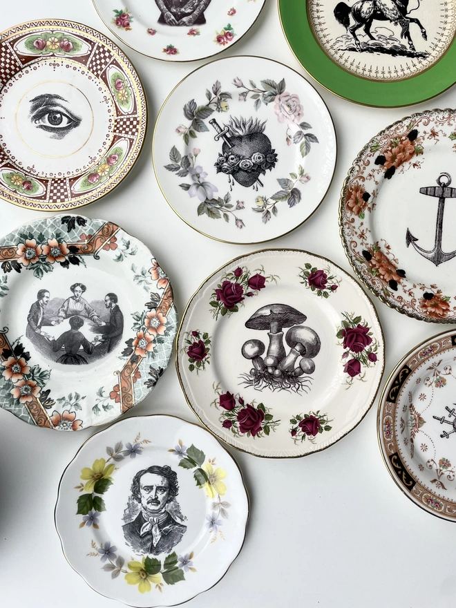 an eclectic collection of vintage plates hung together on a white wall, each plate is different with patterned or gold borders and vintage images in their centres