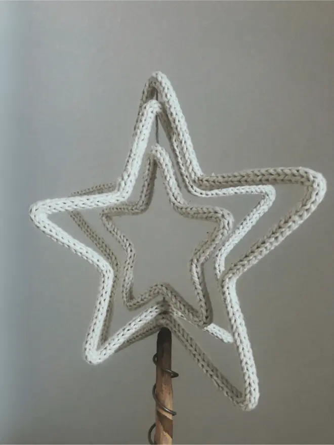 Knitted string & wire Triple Star tree topper atop a stick against an off white background