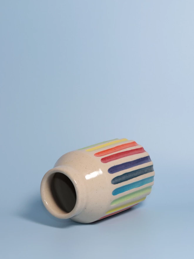 Rainbow striped pottery bud vase laying on its side, open end facing camera