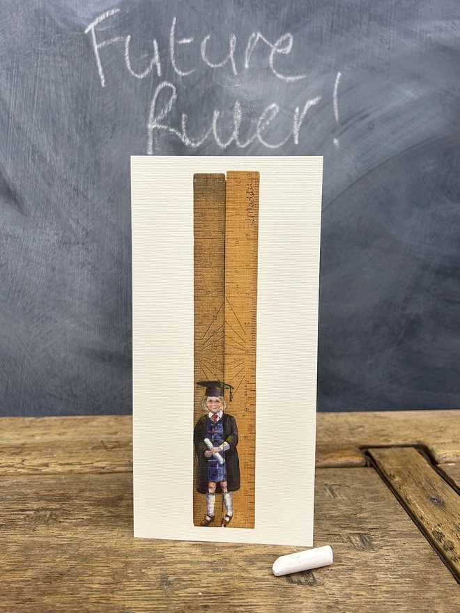 little girl wearing a graduation gown and cap standing in front of school rulers