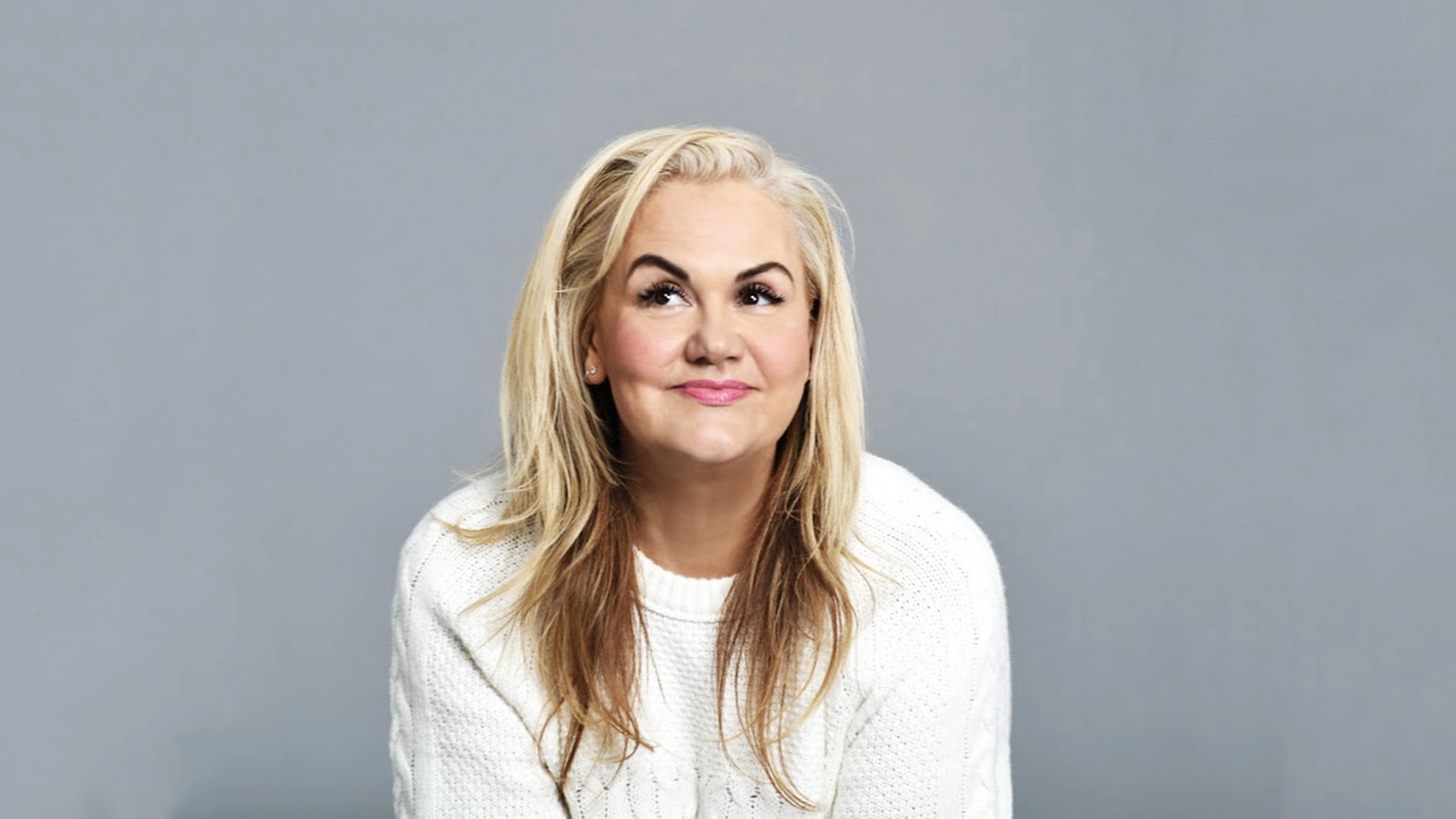 Caroline Hirons, youtuber and founder of Caroline Hirons, smiling above the camera, sat infront of a grey background.