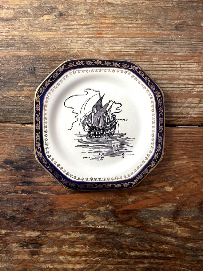 vintage plate with an ornate border, with a printed vintage illustration of an ghost ship in the middle 