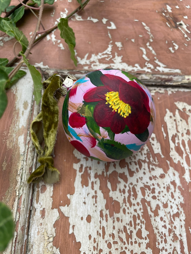 hand painted ceramic christmas bauble background pale pink adorned with deep red camellia flowers