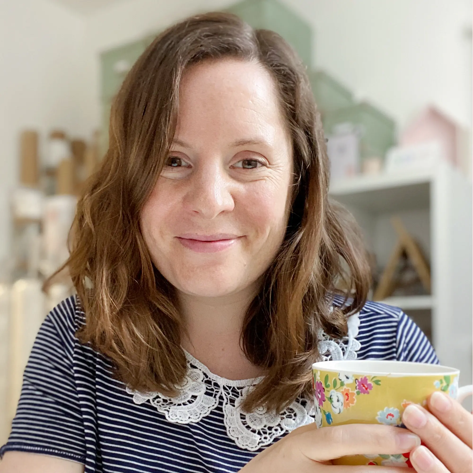 Laura Clempson the founder of Clara and Macy sits in her office, holding a cup of tea and wearing a blue striped top with lace collar.