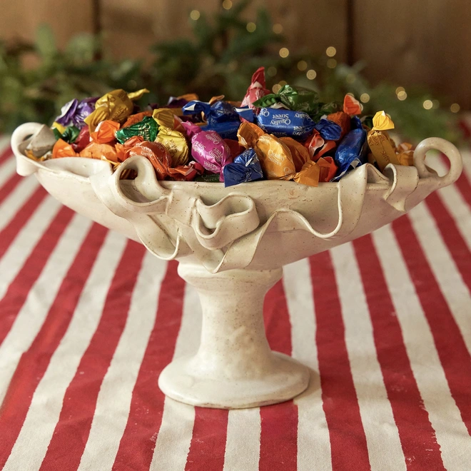 Ceramic bow vase filled with quality street on a red striped tablecloth