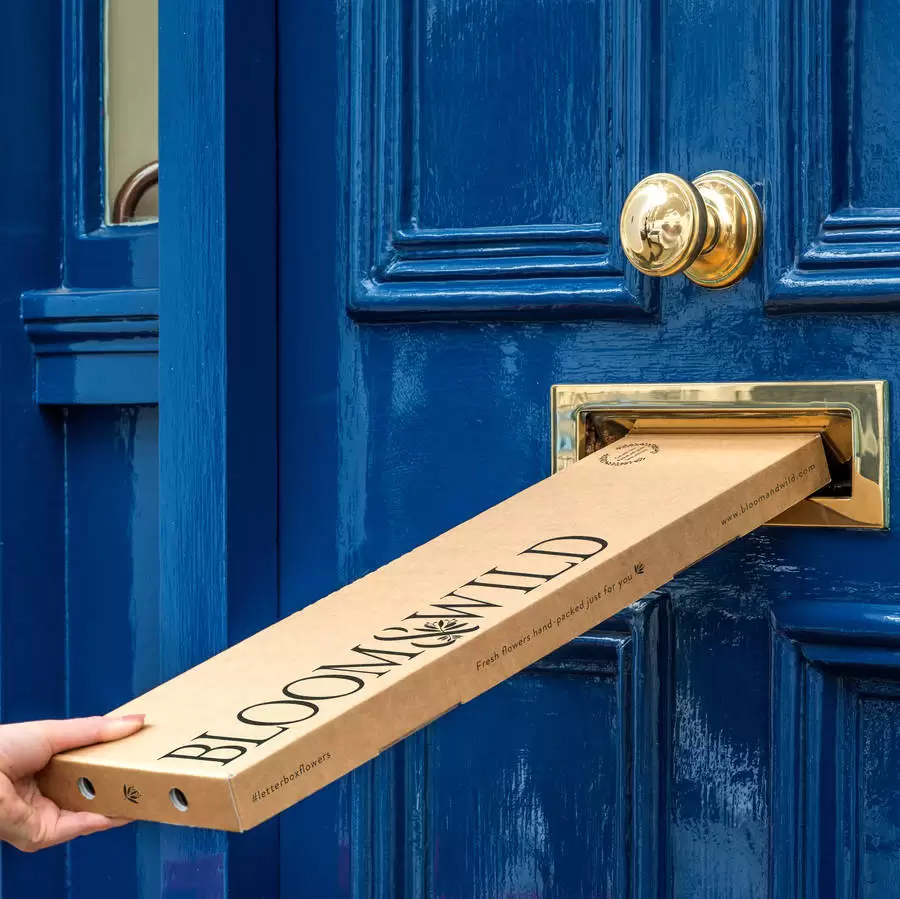 Letterbox flowers from Bloom & Wild being posted through a blue door with gold letterbox 