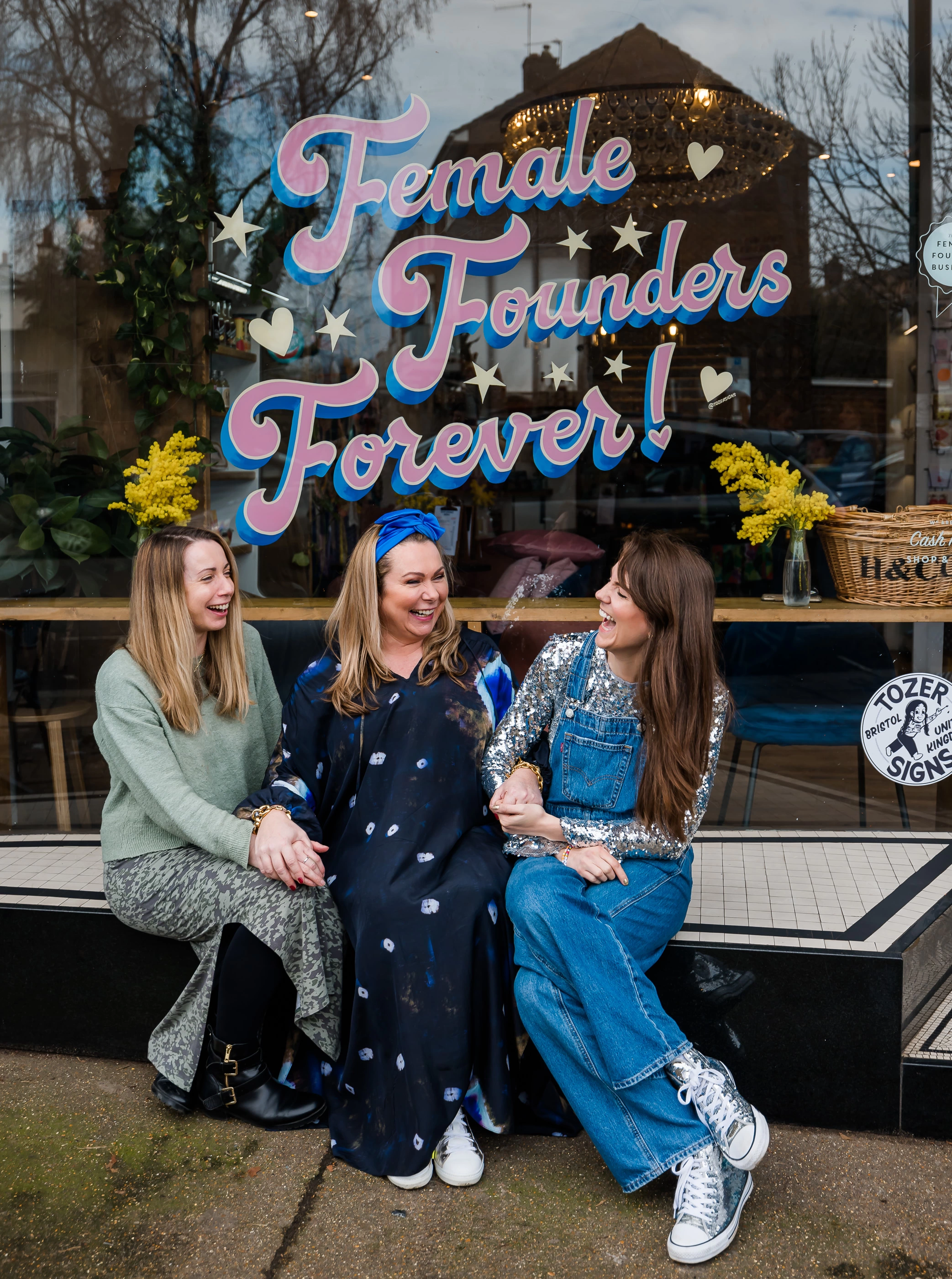 Holly, Carrie and Gabi, founders of Holly & Co, outside a shop window that says 'female founders forever'