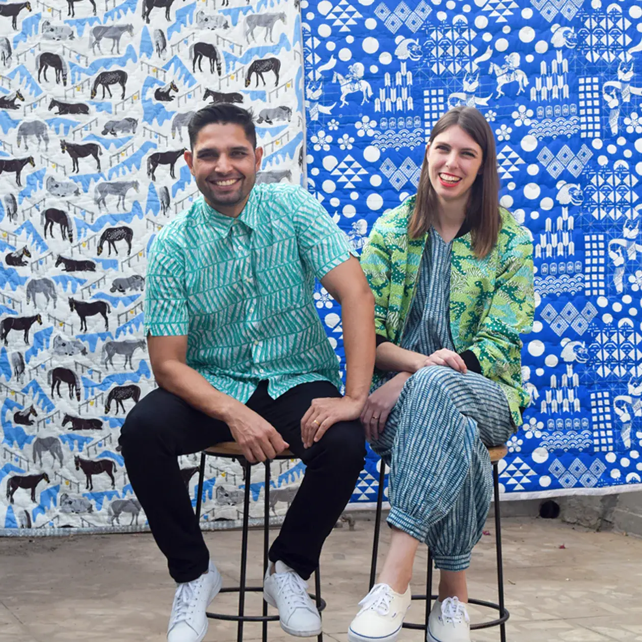 Safomasi founders smiling at camera, sitting on stools in front of patterned fabric hangings