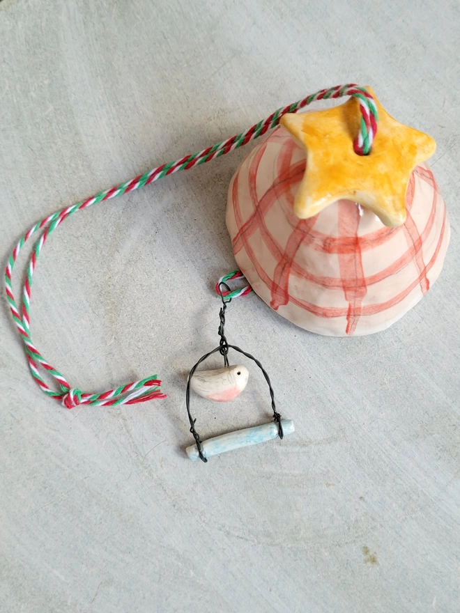 flat lay of a ceramic red and pink check hanging bell with orange star bead on top and a tiny pink budgie bead on a swing