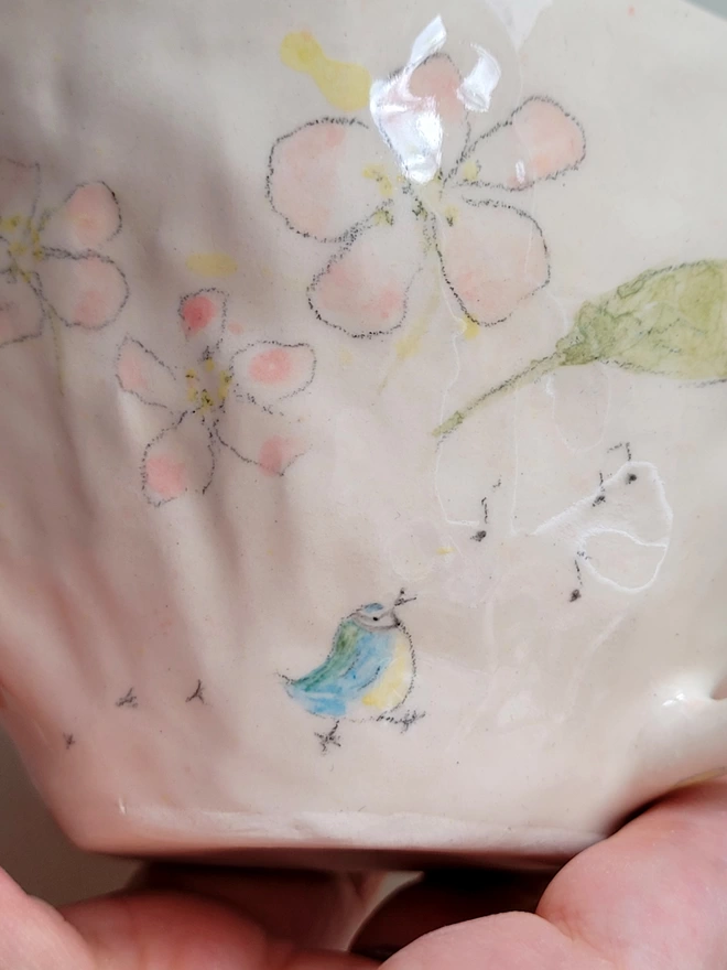 close up of a hand painted blue tit on a mug with whistled musical notes and bird prints with pink apple blossom above
