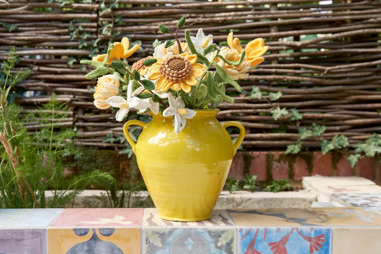 Crochet yellow flowers in a bright yellow vase outside