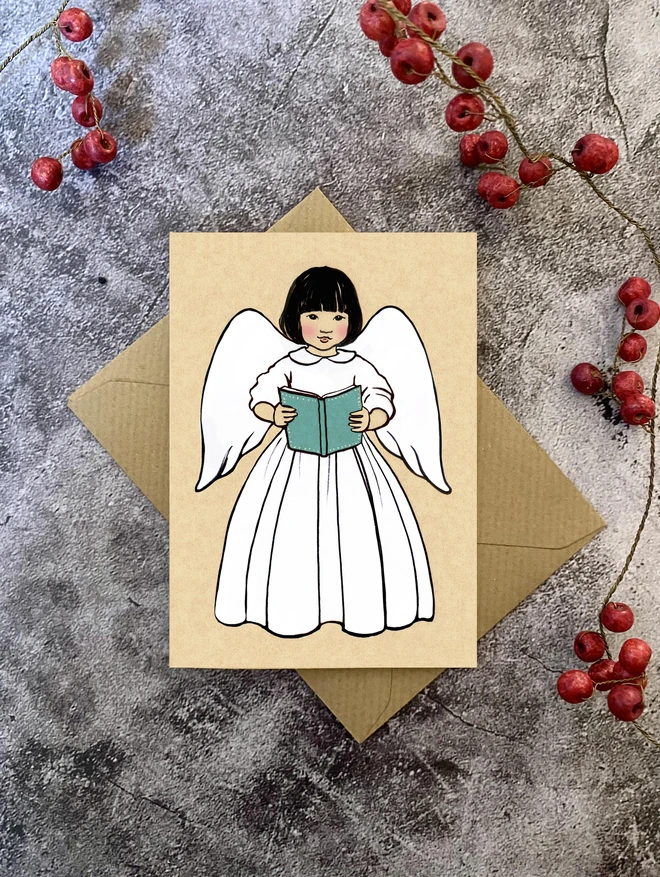 a greeting card showing a Japanese girl angel holding a blue hymn book laid on a Kraft envelope