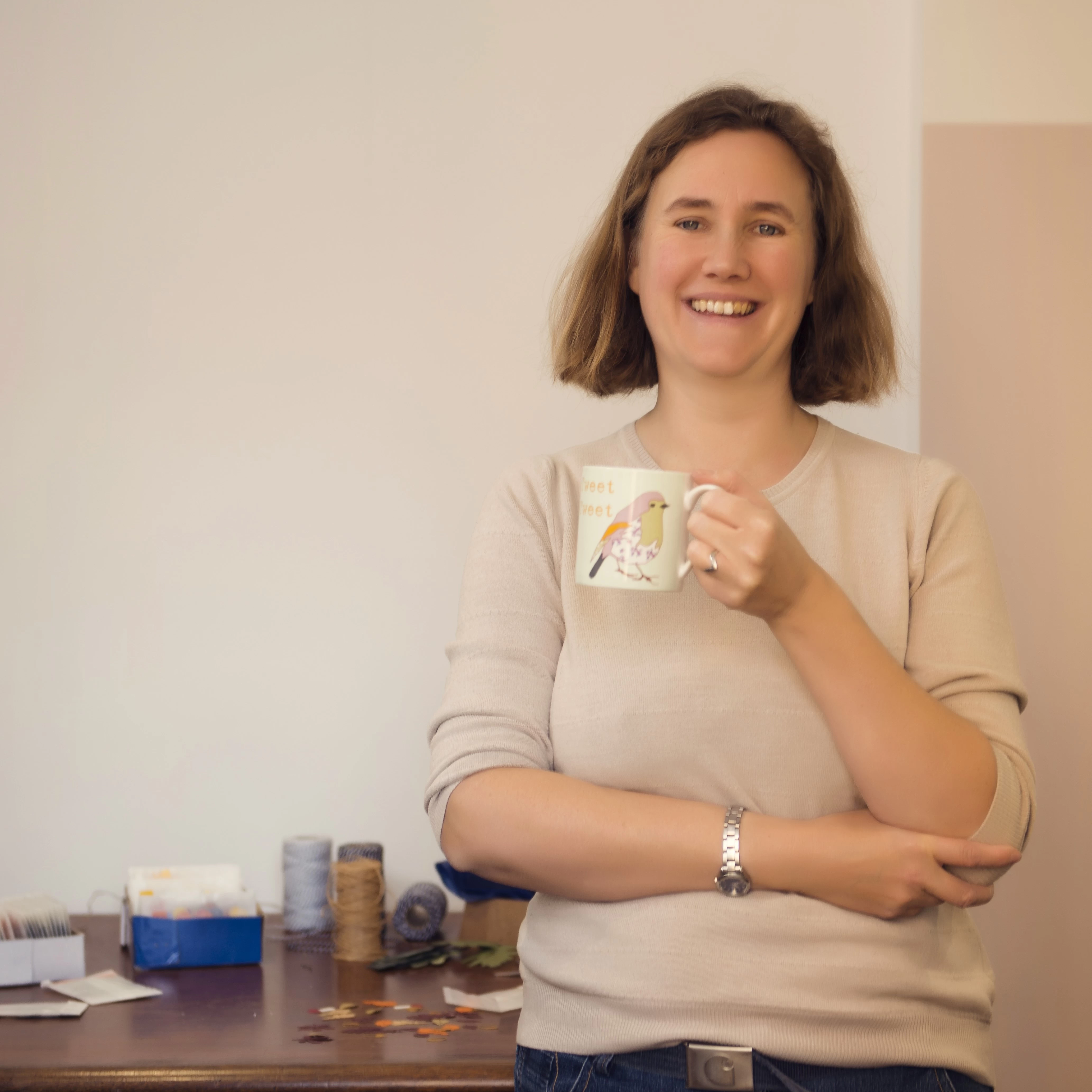 Rosie standing in front of her studio work bench, smiling  and holding a mug of tea
