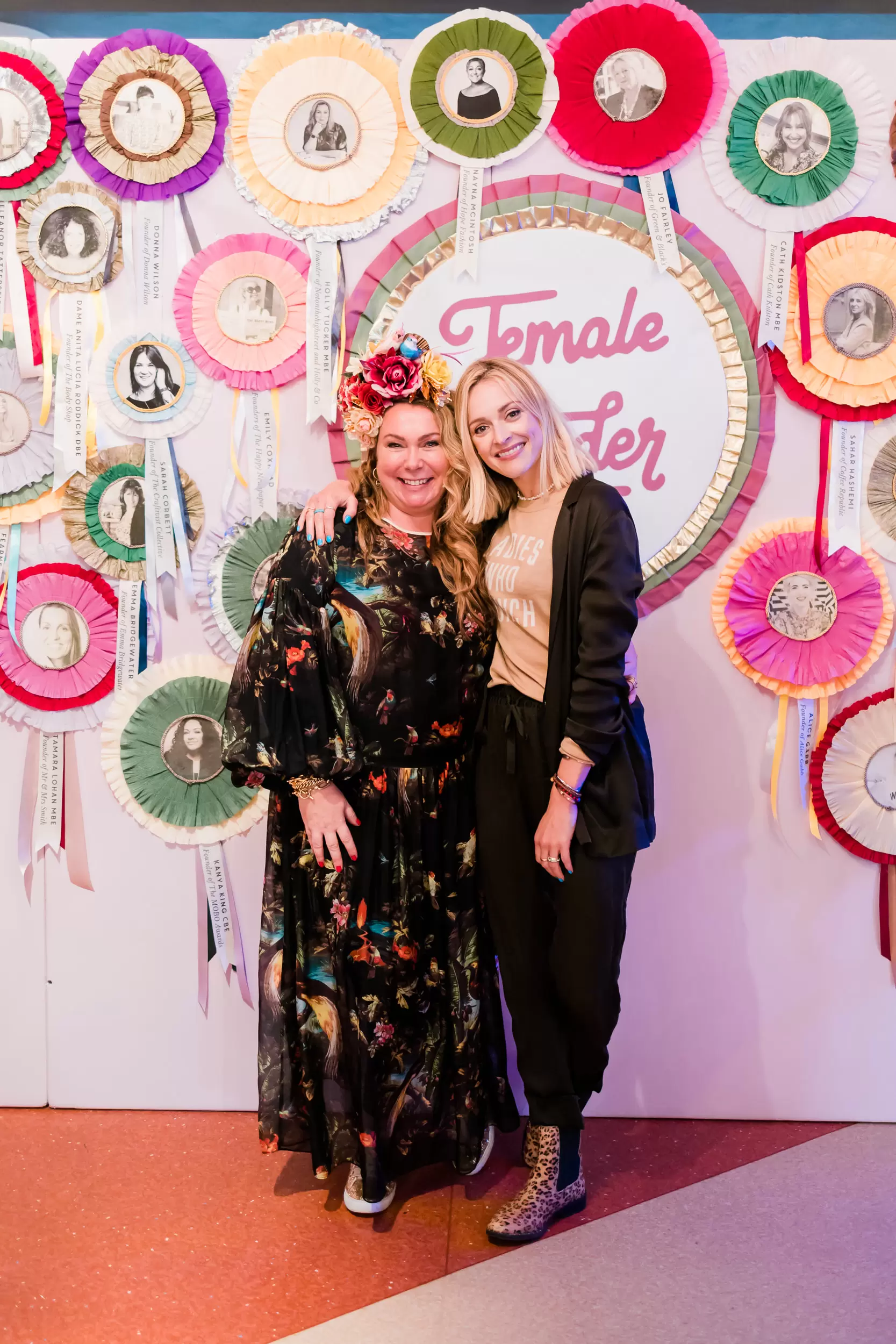 Holly Tucker MBE and Fearne Cotton stood in front of Female Founder rosette wall