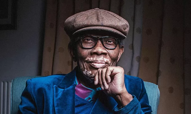 Wilfred Emmanual-Jones MBE, founder of The Black Farmer, smiling at the camera, wearing a blue velvet suit and a baker boy hat.