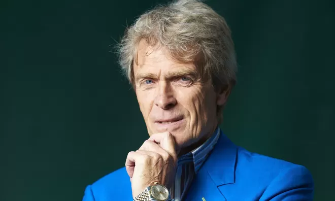 John Hegarty, founder of BBH and The Garage Soho, looking at the camera infront of a green background.