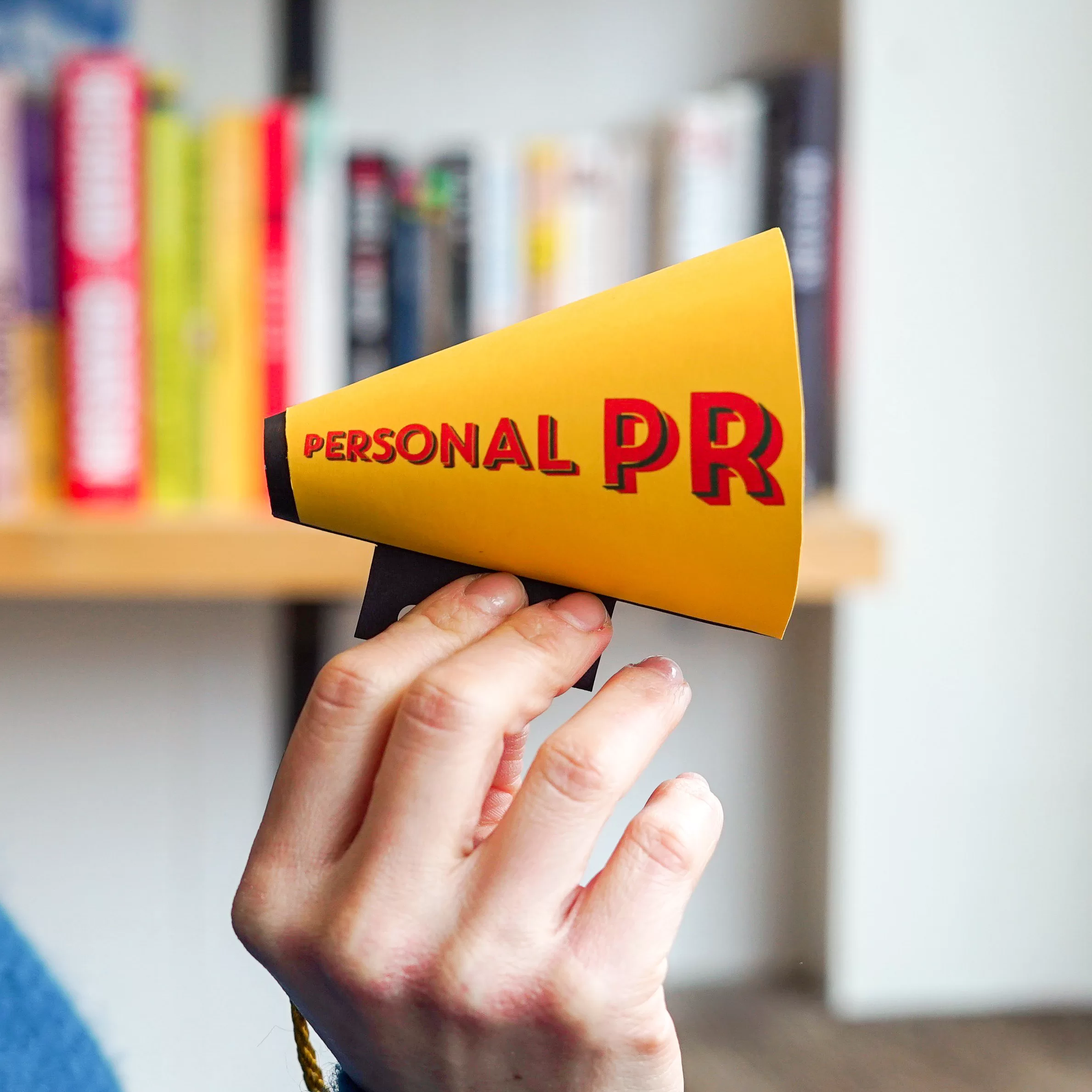 Hand holding up a mini yellow megaphone with the words personal PR written on it
