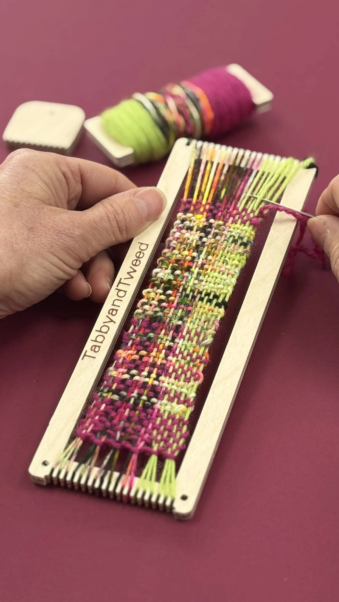 wooden bookmark loom with bright coloured yarn on a pink background
