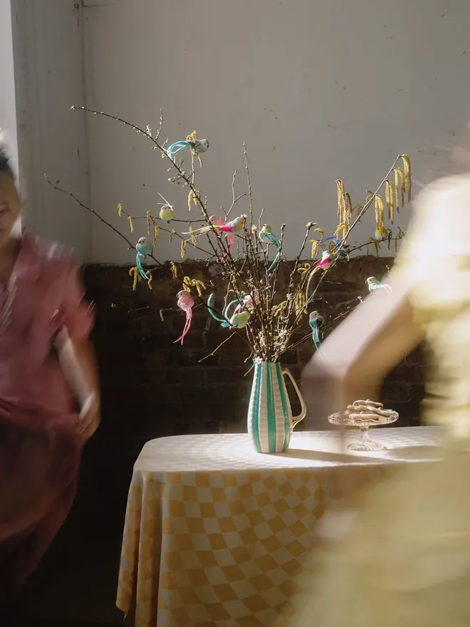 Bird and butterfly clips on blossom display in vintage stripe jug on a tablecloth.