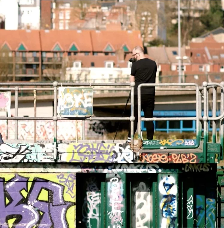 Jayson Lilley standing on a platform covered in graffiti with a camera on a tripod