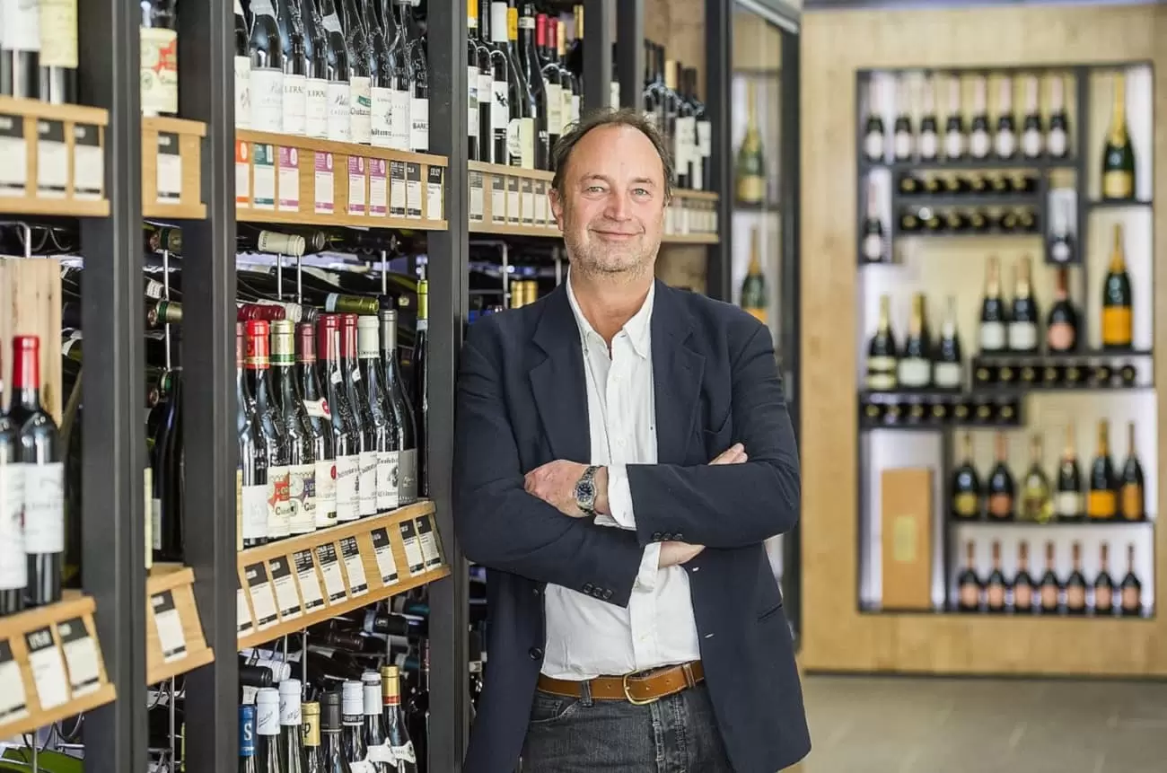 Rowan Gormley, founder of Naked Wines, smiling at the camera infront of a wine rack.