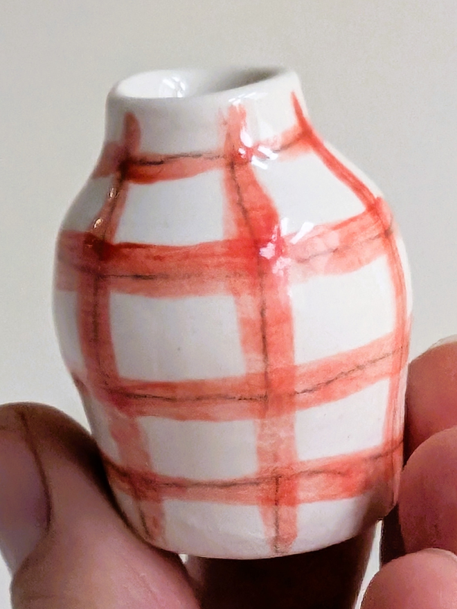 Miniature vase with hand painted red check held in the fingertips