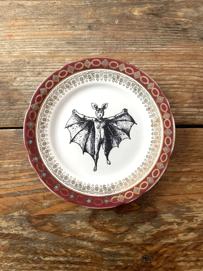 vintage plate with an ornate border, with a printed vintage illustration of a bat boy in the middle 