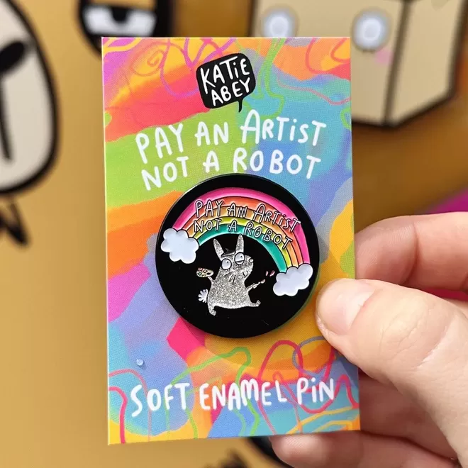 Katie Abey enamel pin saying 'play like an artist not a robot'