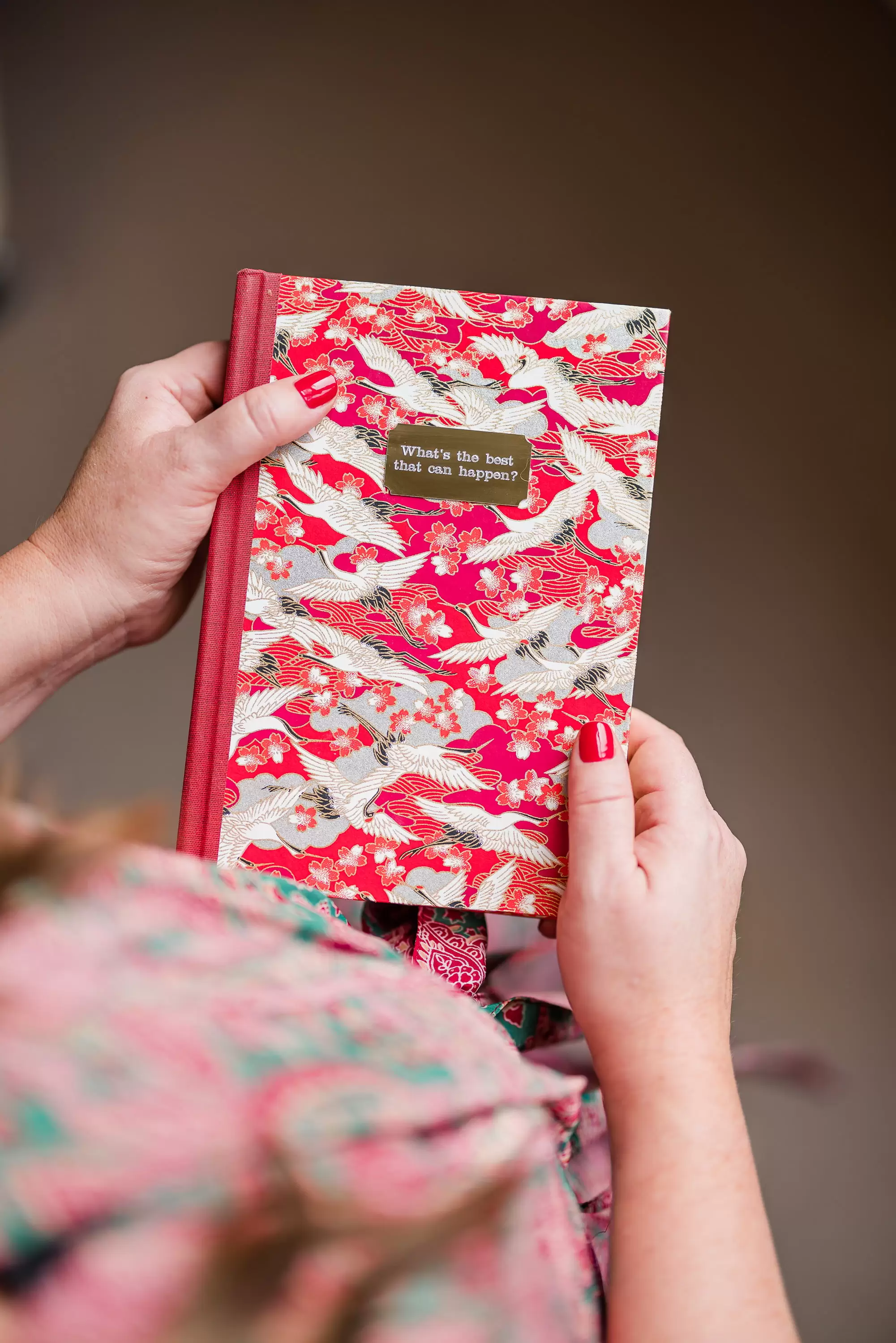 Hands holding a red and white marbled notebook with the words what's the best that can happen on the front