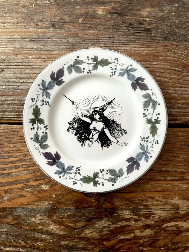 vintage plate with an ornate border, with a printed vintage illustration of a Victorian witch in the middle 