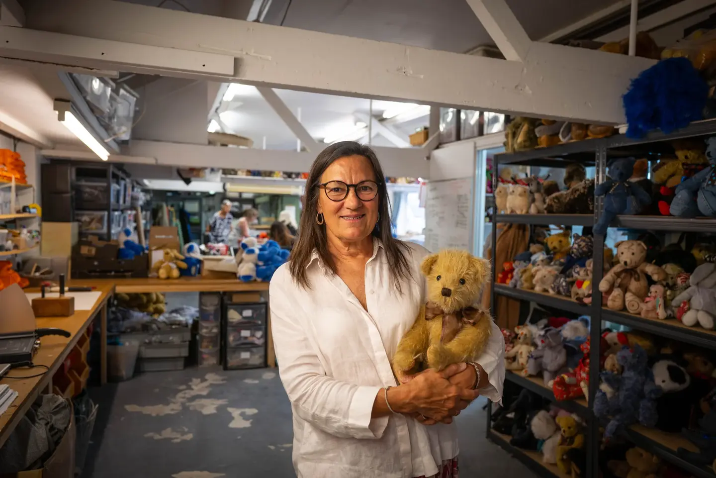 Kerstin holding a teddy bear, in a workshop full of other teddies