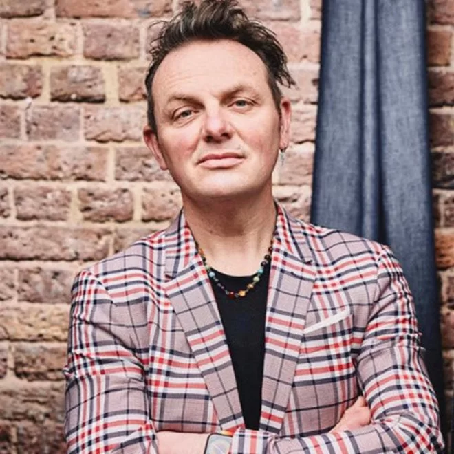 Mark Shayler, thinker, doer, speaker and author, looking at the camera, stood infront of a brick wall.