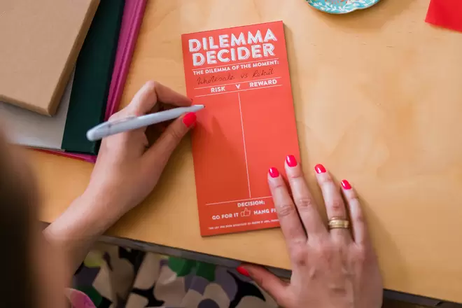Dilemma Decider note pad in orange with woman writing notes 