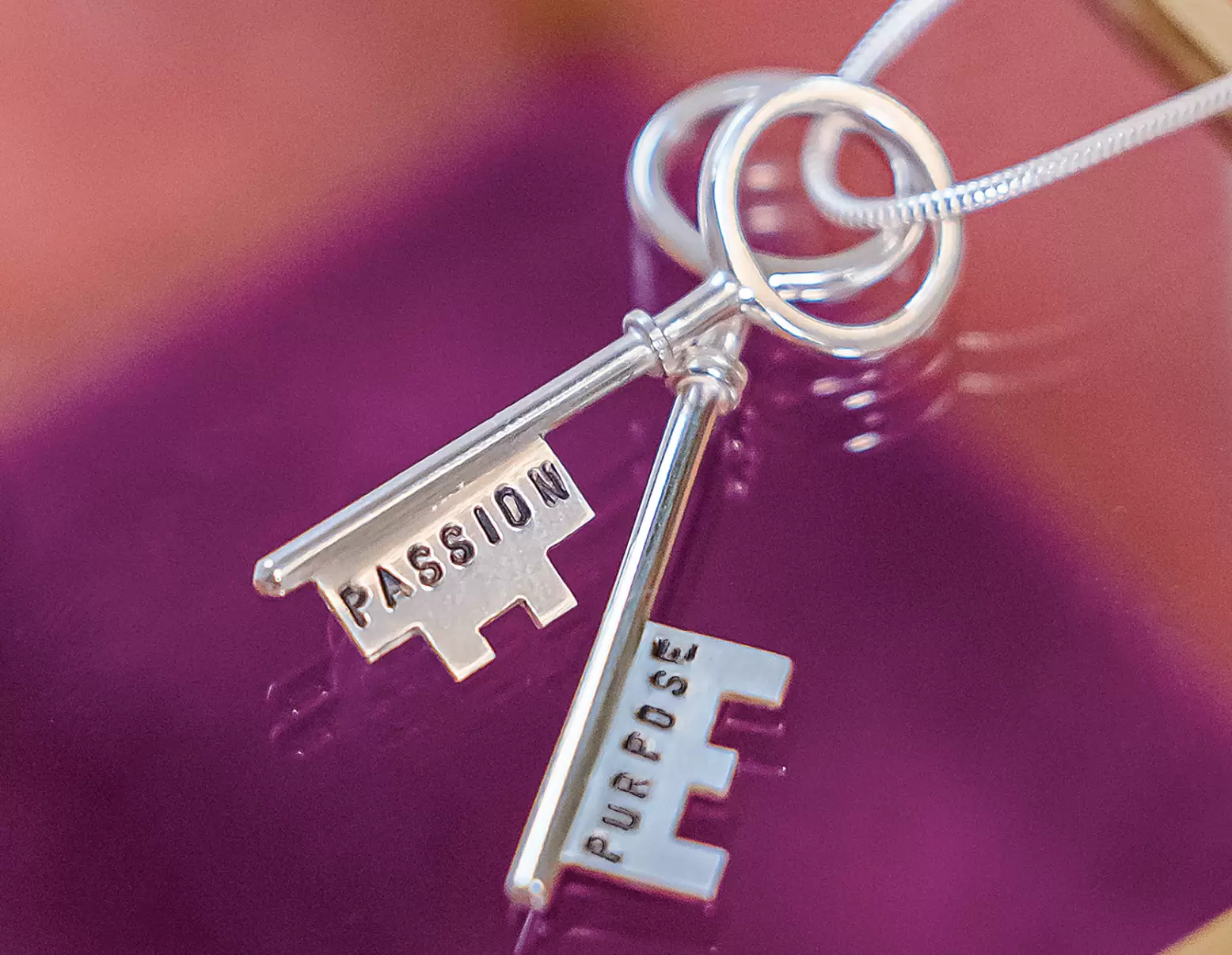 Passion and Purpose key necklace seen against a purple and pink background.