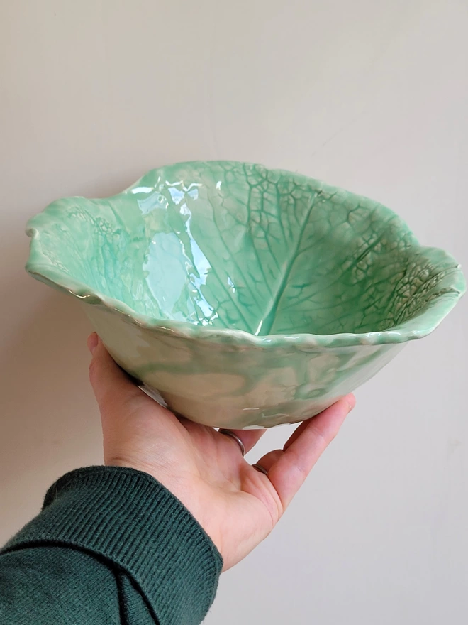 a green cabbage leaf pottery bowl held in a hand showing the green translucent glaze