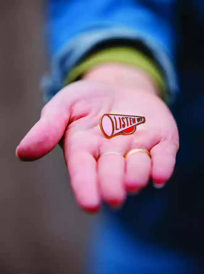 Hand out-stretched holding a Listen Up Pin Badge 
