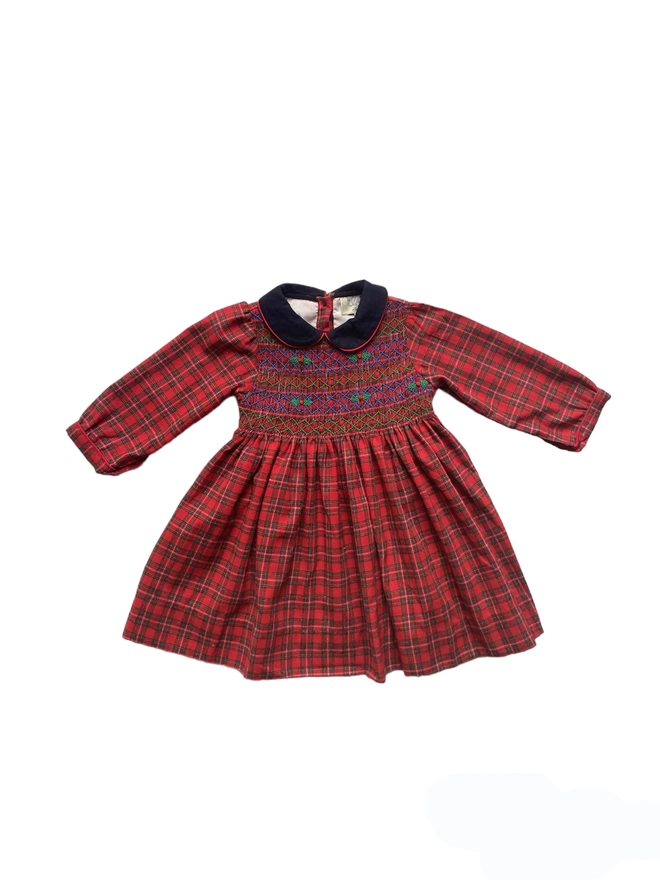 A red tartan dress with a navy collar and hand smocked detailing featuring holly embroidery