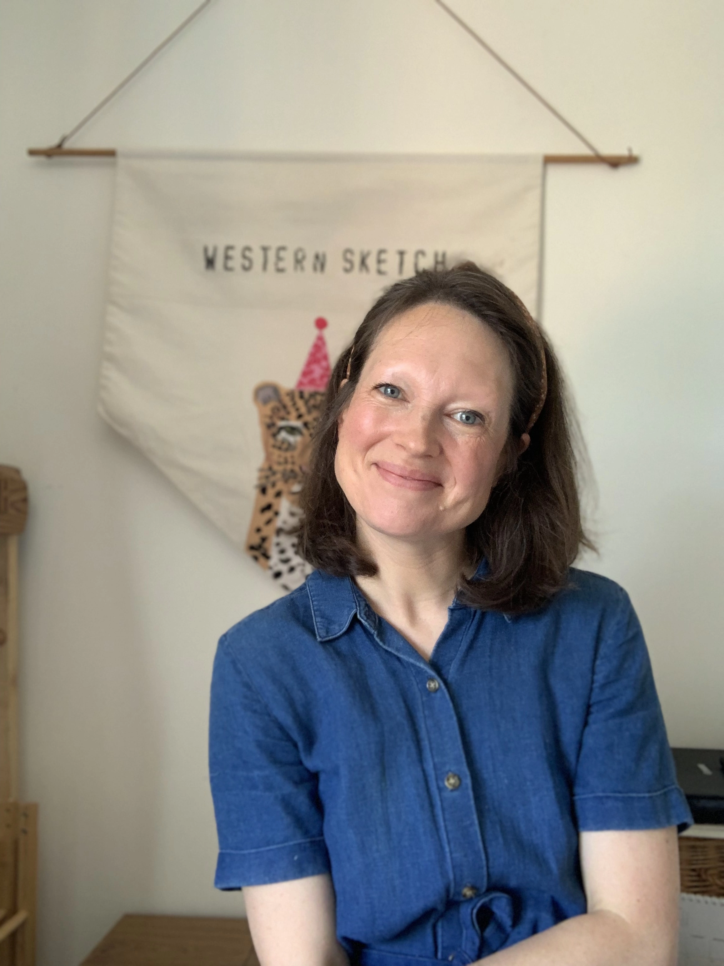 Photograph of Melissa The Illustrator Behind Western Sketch Greeting Cards Sitting In front Of Her Leopard Business Banner  