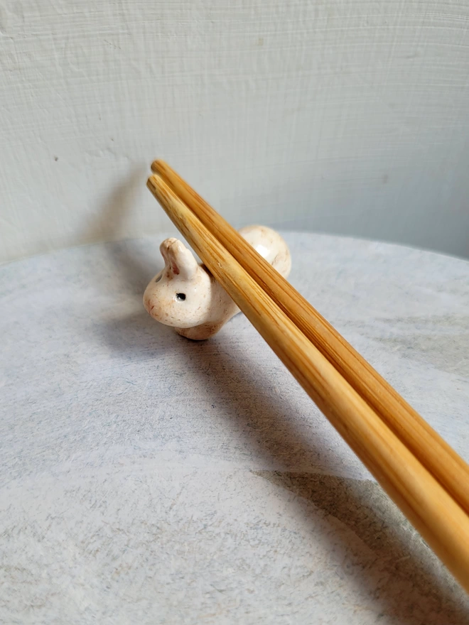 ceramic pottery bunny rabbit figurine designed to rest chopsticks on with a pair of bamboo chop sticks resting on top of it