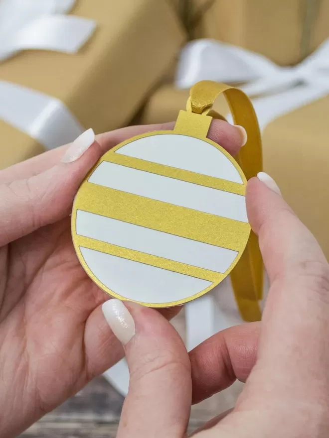 Model holds gold and white round bauble gift tag.Gold and White Christmas Bauble Gift Tag
