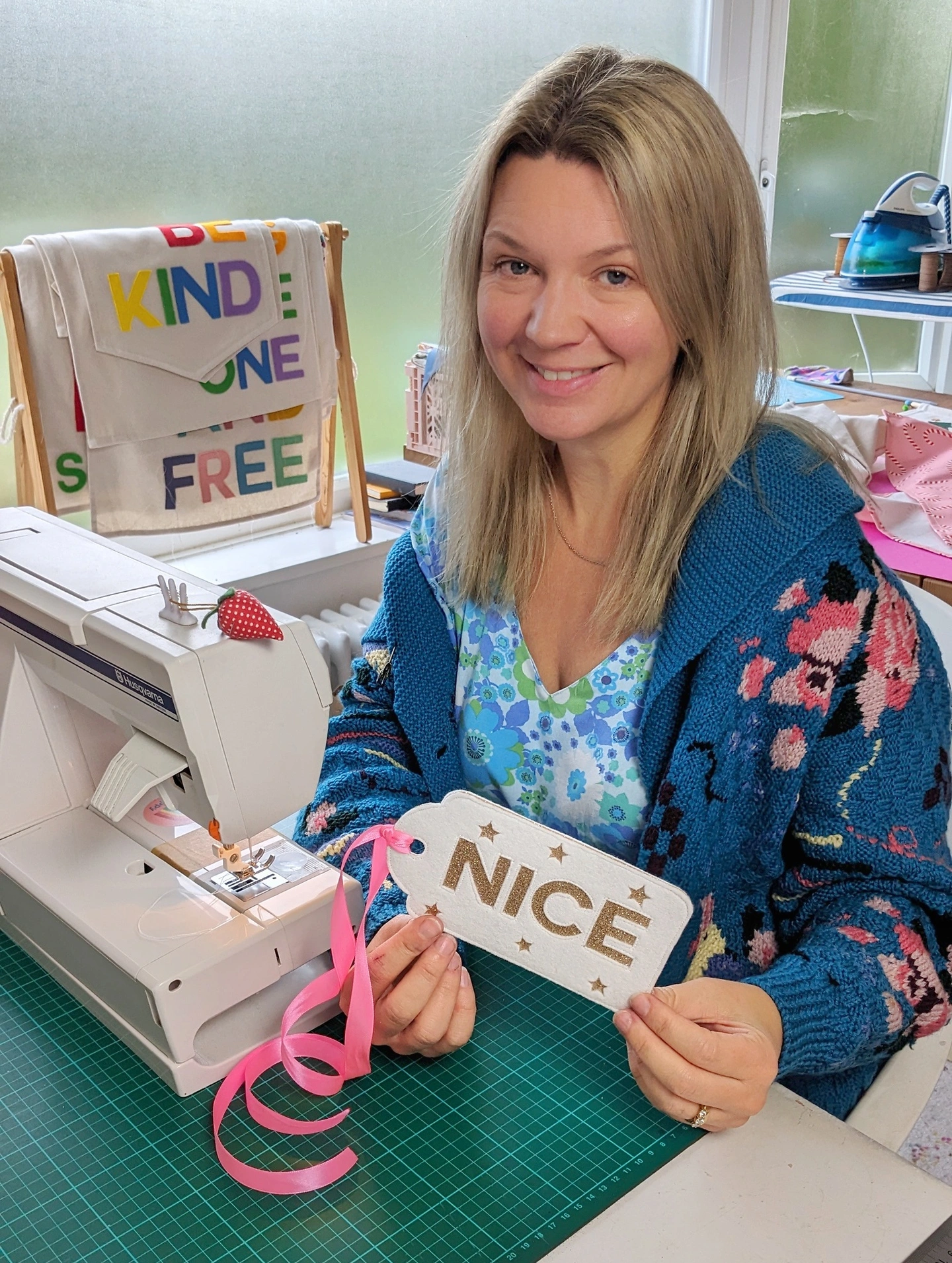 Colourful photo of a woman sat at a sewing machine with colourful banners in the background