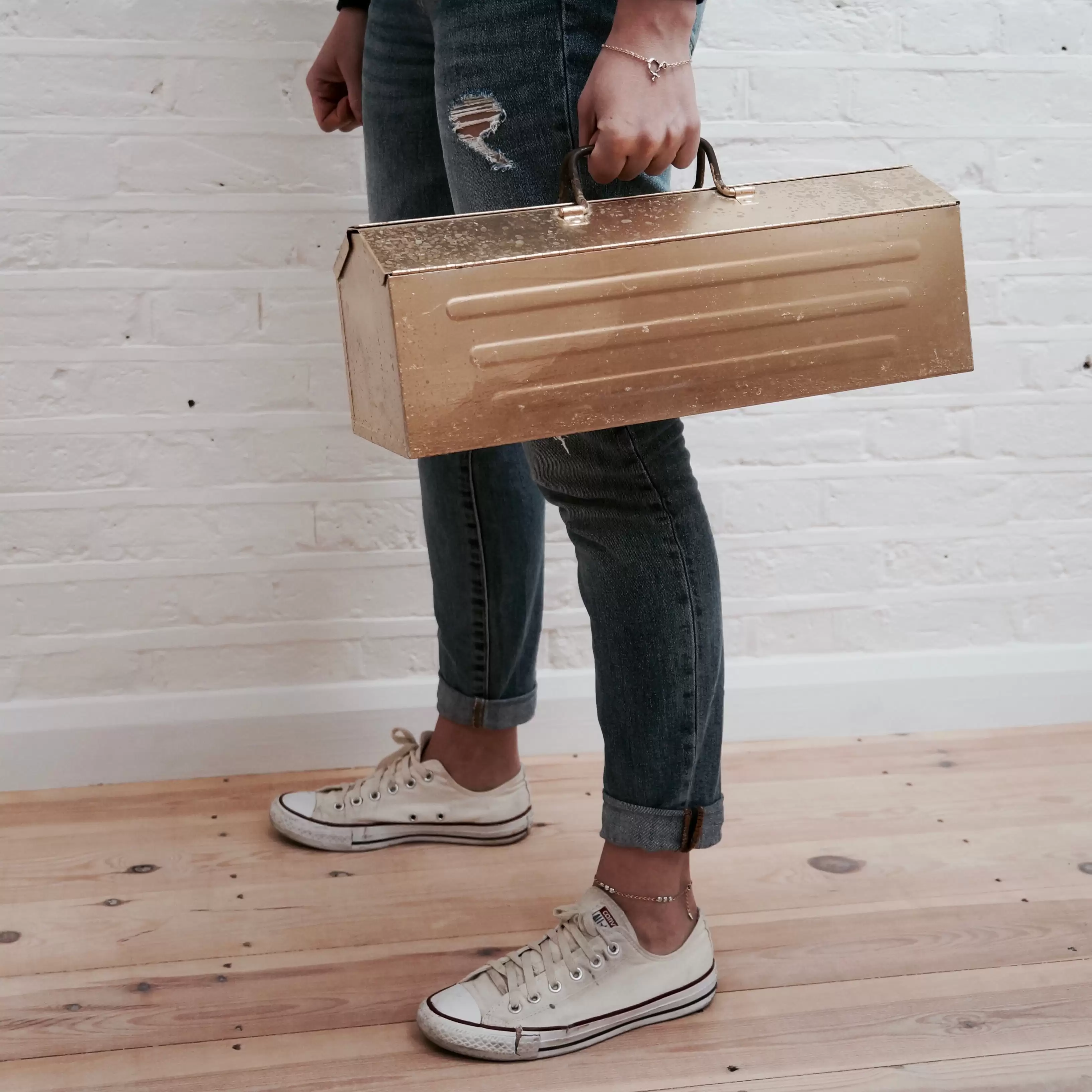 Woman wearing black jeans holding gold toolbox 