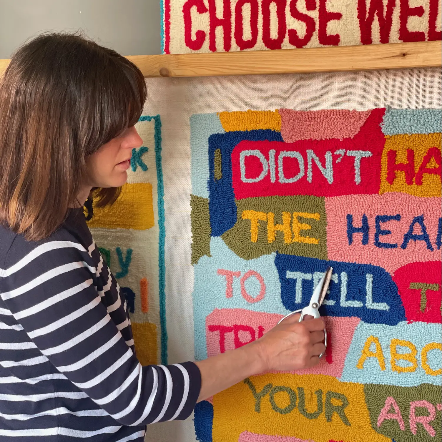 Lady in stripy blue and white top cutting a bright textile artwork with scissors. 