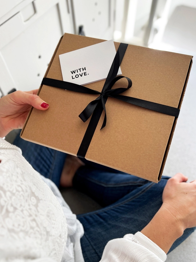 Brown gift box tied up with a black ribbon with a 'With Love' note card places in the ribbon.