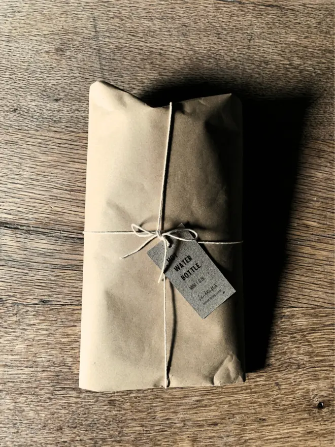 Mini Hot Water Bottle wrapped in brown paper tied with string on an oak table