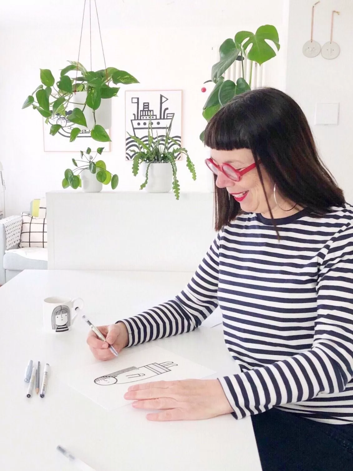 Jane sat at a desk drawing an illustration smiling wearing bright red frames