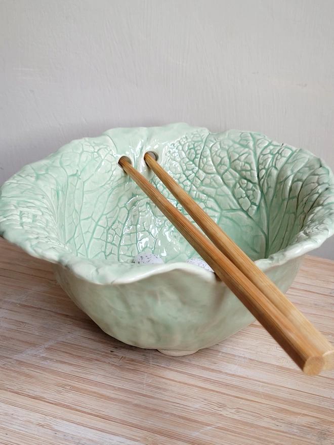 green pottery ramen noodle bowl with chopstick holes and chopsticks resting on top
