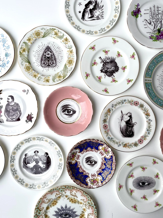 an eclectic collection of vintage plates hung together on a white wall, each plate is different with patterned or gold borders and vintage images in their centres