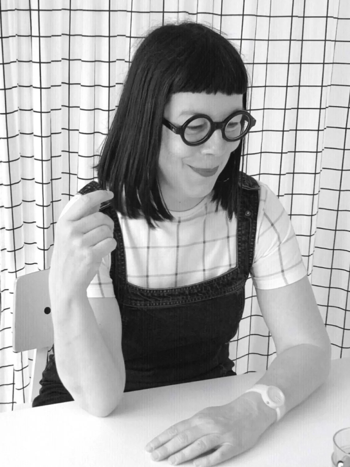 Jane sitting at a desk in black and white smiling whilst wearing thick black glasses